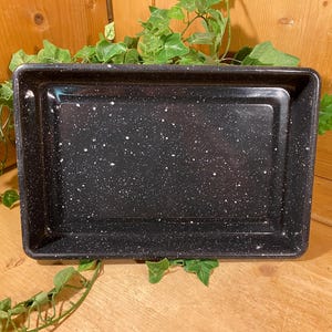 May include: A rectangular baking pan with a black enamel finish and a white speckled pattern. The pan features a smooth, glossy surface with raised edges and a flat base, designed for oven use with a durable, heat-resistant construction.