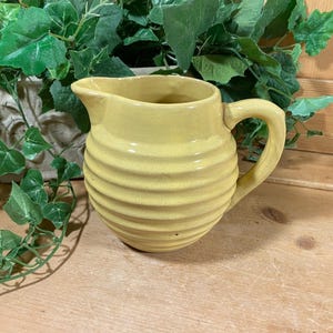 May include: A yellow ceramic pitcher with a ribbed design. The pitcher has a handle and a spout.