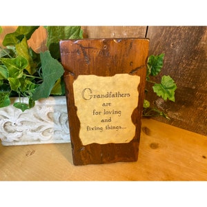 May include: A wooden sign with a beige paper insert that reads "Grandfathers are for loving and fixing things..." The sign is brown and has a rustic look.