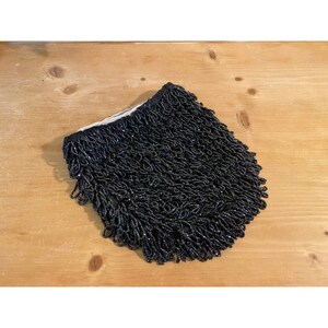 May include: Black beaded fringe trim. The fringe is made of small, black beads that are sewn together to create a thick, luxurious look.