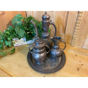 May include: A silver serving set with three pieces, including a pitcher, a creamer, and a sugar bowl, all with intricate designs. The set is displayed on a silver tray with a decorative border.