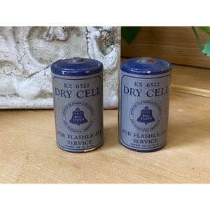 May include: Two vintage silver and blue dry cell batteries with the text "KS 6522 DRY CELL" and "AMERICAN TELEPHONE & TELEGRAPH CO. BELL SYSTEM AND ASSOCIATED COMPANIES FOR FLASHLIGHT SERVICE MADE IN U.S.A."