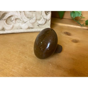 May include: A brown ceramic knob with a smooth, rounded top and a black base. The knob has a speckled appearance.
