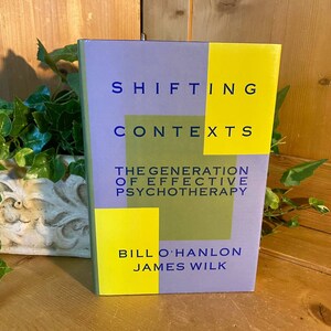 May include: A purple book with a yellow and green cover. The title is "Shifting Contexts: The Generation of Effective Psychotherapy" by Bill O'Hanlon and James Wilk.