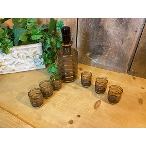 May include: A set of six brown and gold striped shot glasses and a matching decanter. The glasses and decanter have a frosted glass finish with gold stripes.