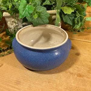 May include: A blue ceramic casserole dish with two handles. The dish has a white interior and a speckled blue glaze.