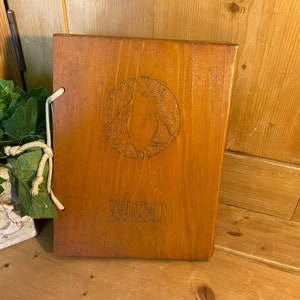 May include: A wooden menu cover with a carved penguin design and the word "MENU" on the front. The cover is tied with a white string.