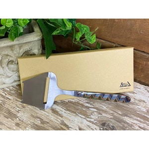 May include: A stainless steel cheese knife with a colorful patterned handle. The knife is in a brown cardboard box with the text "Studio & Gallery" printed on it.