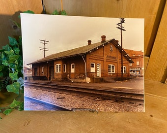 May include: A vintage photograph of a brick train station with the word "Richlands" above the entrance. The station is surrounded by railroad tracks and a few other buildings in the background.