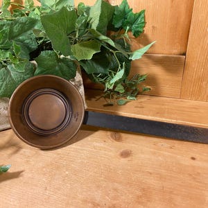 May include: A copper ladle with a black handle. The ladle has a rounded bowl with a slightly raised center.