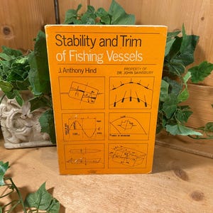 May include: An orange book titled "Stability and Trim of Fishing Vessels" by J. Anthony Hind. The cover features diagrams and the text "PROPERTY OF DR. JOHN SAINSBURY". The book is surrounded by green foliage.