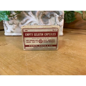 May include: A vintage cardboard box with red lettering that reads "100 Empty Gelatin Capsules No. 4". The box is labeled "Protect from moisture and heat" and "Self locking caps insure tight fit". The box also reads "Heavy shoulders prevent breakage" and "Parke, Davis & Co. Detroit, Mich., U.S.A."
