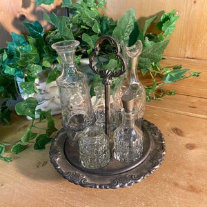 May include: A silver-plated tray with a decorative design holds a set of five glass bottles and jars. The bottles are clear and have a variety of shapes and sizes. The tray is perfect for serving condiments or oils.