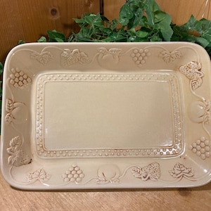 May include: A rectangular, off-white ceramic serving platter with embossed fruit and leaf designs around the border. The center has a slightly recessed area. The platter is decorated with grapes, peaches, and strawberries.