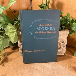 May include: A dark blue hardcover textbook titled Intermediate Algebra for College Students by Thurman S. Peterson. The front cover features light blue text and a thin oval graphic line, with the author's name printed in orange at the bottom.