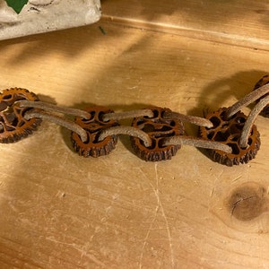 May include: A brown leather bracelet with multiple strands and wooden beads. The beads are carved with intricate designs and have a natural, rustic look.
