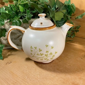 May include: A white ceramic teapot with a brown lid and green shamrock design.