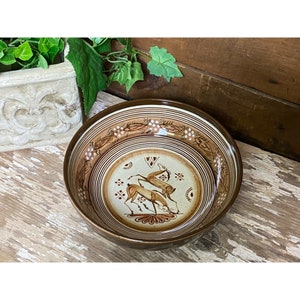 May include: A brown ceramic bowl with a white and brown design featuring two stylized deer. The bowl has a brown rim and a white interior.