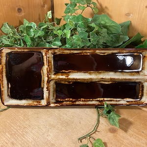 May include: A rectangular ceramic serving tray with three distinct compartments. The tray features a glossy dark brown glaze in the center of each section, contrasted by a textured, lighter tan and cream drip glaze along the raised edges.