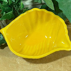 May include: A bright yellow ceramic bowl shaped like a leaf. The bowl has a smooth, glossy finish and a slightly rippled texture.