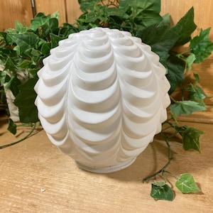 May include: A spherical white glass light shade featuring a repeating molded scalloped or petal-like pattern across its surface. The globe has a circular opening at the base for mounting and a smooth, matte finish that diffuses light across the texture.