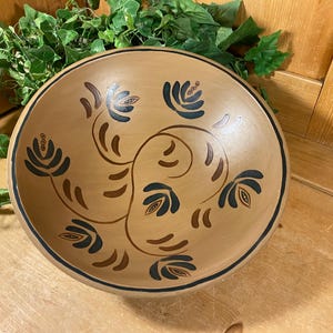 May include: A round, wooden bowl with a light brown finish. The bowl features a dark blue and brown floral design around the rim and center. The rim is outlined with a dark blue band. Decorative kitchenware.