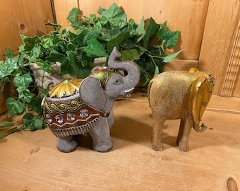 May include: Two decorative elephant figurines. One is gray with gold and green accents and rhinestones. The other is gold.