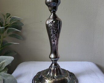 May include: A silver candlestick with an ornate design. The base and stem are decorated with intricate floral patterns. The candlestick is tall and slender, with a round base.