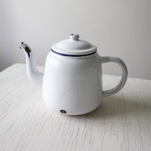 May include: White enamel teapot with a blue rim and a small spout. The teapot has a rounded body and a handle on the side.