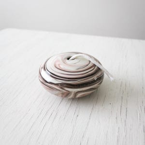 May include: A round pull with a marbled effect in shades of brown, white, and pink. A white cord emerges from a hole at the top. The pull is on a white, textured surface.