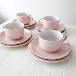 May include: A set of four pink teacups and saucers. The cups and saucers have a subtle, rippled texture. The cups have a white interior.