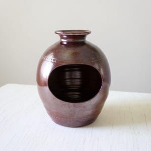 May include: A brown ceramic pot with a large opening on one side. The pot has a smooth, glossy finish and a slightly rounded shape.