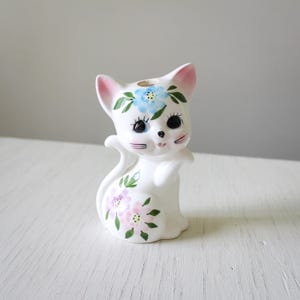 Peut inclure: Figurines de chat en céramique blanche avec des fleurs peintes roses et bleues. Le chat a de grands yeux noirs et un nez rose.