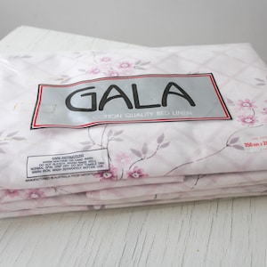 May include: A folded set of Gala cotton quality bed linen in a clear plastic package. The sheets have a light pink floral pattern with a diamond grid design. The package dimensions are 98 x 78 inches and 19 x 29 inches.