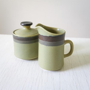 May include: A green and brown ceramic creamer and sugar bowl set with a striped design. The creamer has a handle and the sugar bowl has a lid.