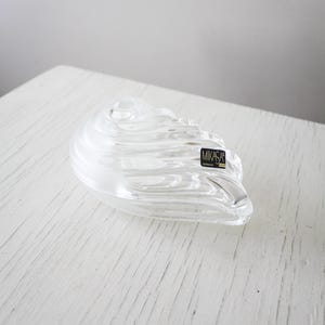 May include: Clear glass decorative bowl with a swirling design. The bowl has a unique shape and a sticker that reads "MIKASA Germany". The bowl is sitting on a white surface.