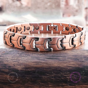 Könnte beinhalten: Ein kupfernes Magnetarmband mit schwarzem Akzent. Das Armband hat einen Verschluss und besteht aus mehreren Gliedern.