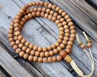 May include: A brown wooden mala bead necklace with a tassel. The beads are round and have a natural wood finish. The tassel is made of a braided cord with a gold metal accent.