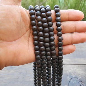 May include: A close-up of a strand of dark brown wooden beads. The beads are round and smooth, and they are strung together on a thin cord. The beads are arranged in a straight line, and they are all the same size.