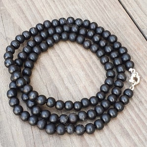 May include: A black wooden beaded necklace with a silver clasp. The beads are round and smooth, and the necklace is approximately 18 inches long.