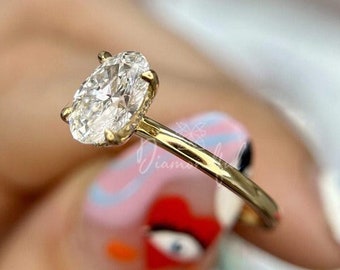 Puede incluir: Un anillo de compromiso de oro con un diamante de forma ovalada. El anillo está en un dedo con esmalte de uñas de colores.