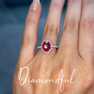 May include: A ring featuring an oval-cut deep red ruby centre stone surrounded by a halo of small white diamonds on a thin metallic band. The word Diamondful is written in white cursive script across the lower portion of the image.