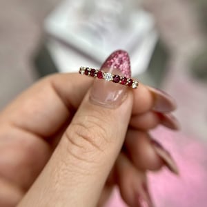 以下が含まれることがあります： 中央にダイヤモンドが1つ、両側にルビーが並んだ、繊細なゴールドのバンドリングです。