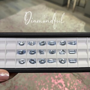 Op de afbeelding: Een zwarte tray met lichtblauwe edelstenen in verschillende vormen, waaronder ovaal en rechthoekig. Het woord "Diamondful" is in sierlijke letters geschreven.