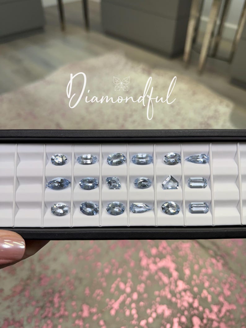 Op de afbeelding: Een zwarte tray met lichtblauwe edelstenen in verschillende vormen, waaronder ovaal en rechthoekig. Het woord "Diamondful" is in sierlijke letters geschreven.