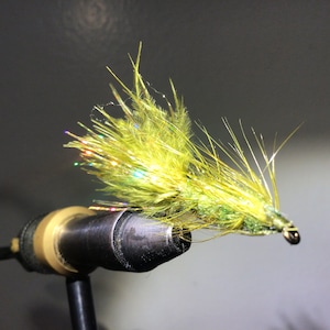May include: A green and yellow fly fishing lure with iridescent fibres tied to a fishing hook.