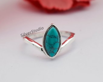 May include: A silver ring with a turquoise marquise-shaped stone. The ring band has a V-shape design. The text "SilverStudio" is visible on the ring. The ring is set against a white background with a red floral accent.