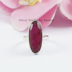 Peut inclure: Une bague en argent avec une grande pierre précieuse en rubis facetté de forme ovale. La bague est sertie sur une simple bande en argent.