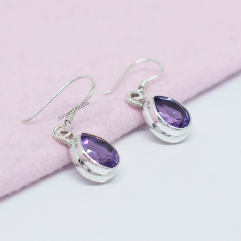May include: A pair of silver dangle earrings with teardrop-shaped amethyst gemstones.