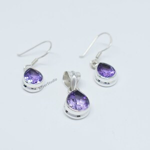 May include: A silver pendant and earrings set with a teardrop-shaped amethyst gemstone. The pendant and earrings have a silver bezel setting.